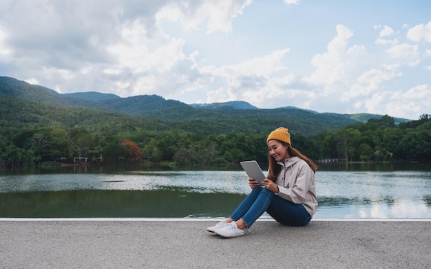 Uma jovem segurando e usando tablet digital enquanto viaja montanhas e lago