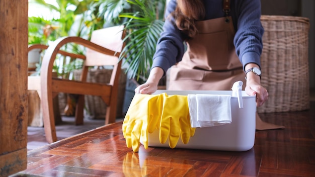 Uma jovem segurando um balde com ferramentas e equipamentos de limpeza em casa