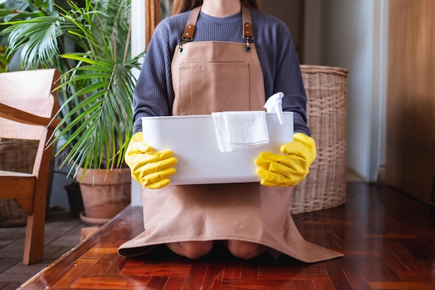 Uma jovem segurando um balde com ferramentas e equipamentos de limpeza em casa