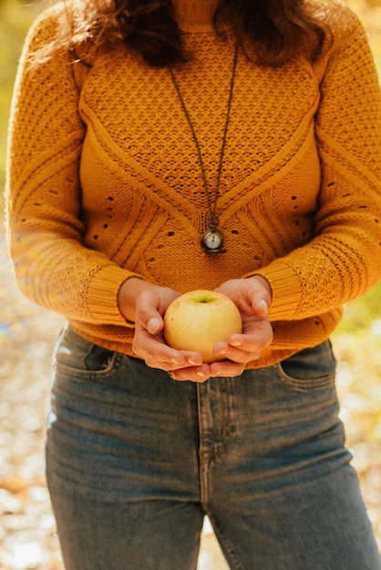 Uma jovem segurando uma maçã no fundo da folhagem em um parque de outono