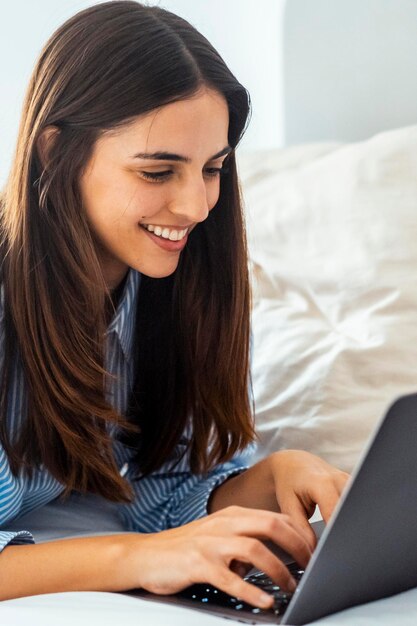 Uma jovem senhora relaxando navegando na rede sozinha em casa deitada na cama no quarto viajante negócios on-line modernos pessoas trabalhando no quarto do hotel uma mulher usando computador portátil com relaxamento