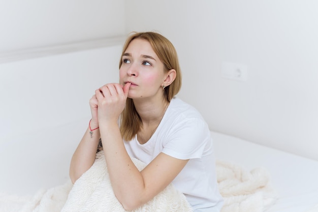 Uma jovem senta-se na cama, preocupa-se e rói as unhas. mulher casual preocupada sentada na cama no quarto