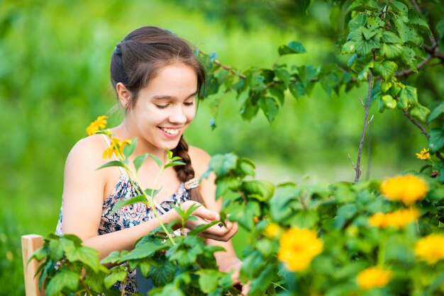 Uma jovem sentada em um jardim perto de um arbusto com flores