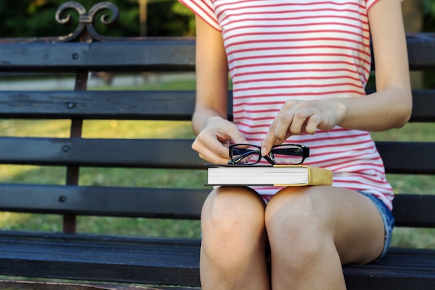 Uma jovem sentada no parque segurando um livro de óculos