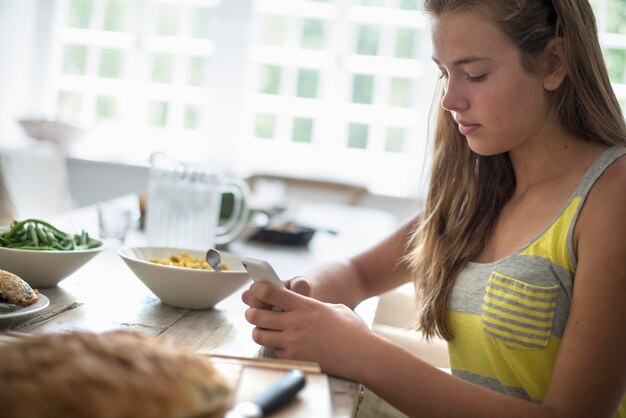 Foto uma jovem sentada verificando seu telefone inteligente em uma mesa de jantar