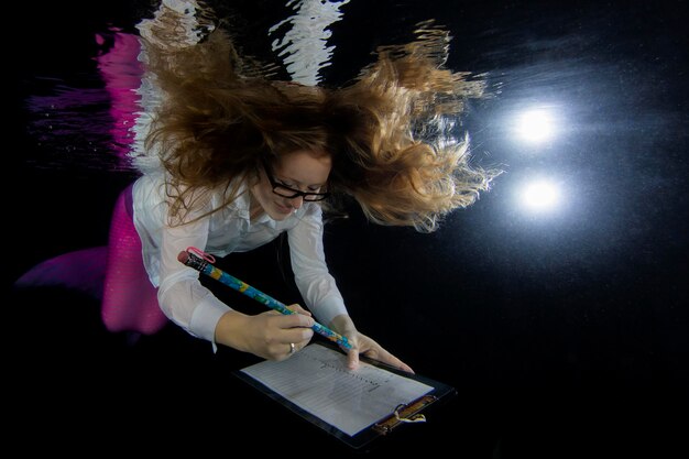 Foto uma jovem sereia sorridente escrevendo enquanto nada debaixo d'água