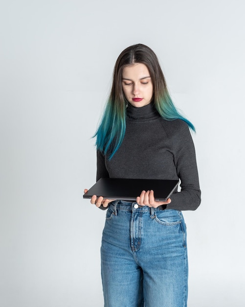 Uma jovem séria e pensativa com cabelo azul é uma estudante universitária segurando um laptop