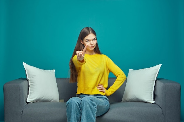 Uma jovem séria faz um sinal de aviso ameaçar com o dedo dando conselhos dizendo que não se sente no sofá
