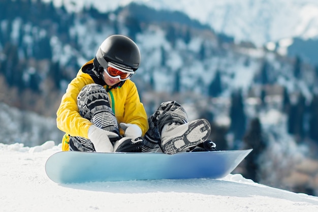 Uma jovem snowboarder senta-se na neve e aperta os fechos de uma prancha de snowboard antes da descida