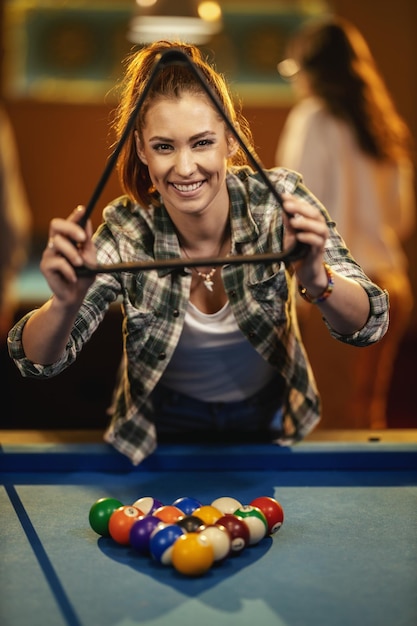 Uma jovem sorridente coloca bolas de bilhar em uma mesa de bilhar para jogar.