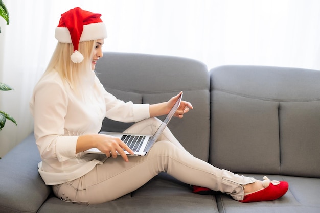 Uma jovem sorridente com chapéu de Papai Noel vermelho fazendo videochamada na rede social com família e amigos no dia de Natal.