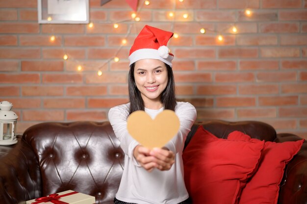 Uma jovem sorridente com chapéu de Papai Noel vermelho, mostrando um modelo em forma de coração no dia de Natal, conceito de férias.