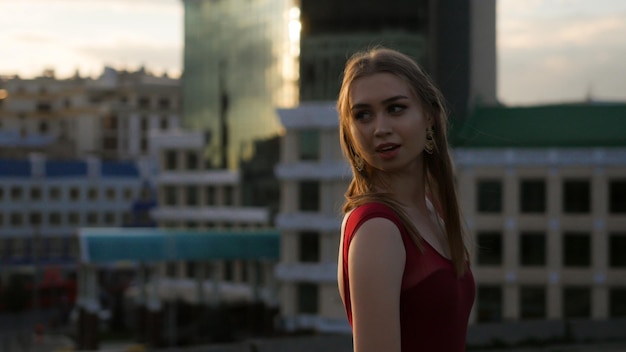 Uma jovem sorridente de vestido vermelho em pé no telhado olhando por trás do ombro