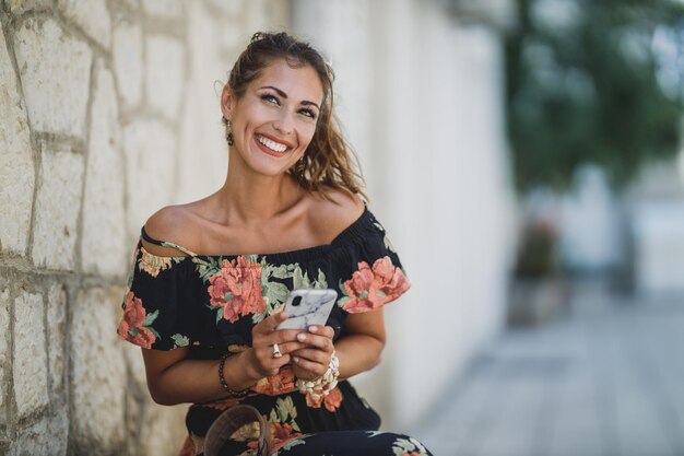 Uma jovem sorridente digitando mensagem em seu smartphone enquanto desfruta de férias de verão na cidade mediterrânea.