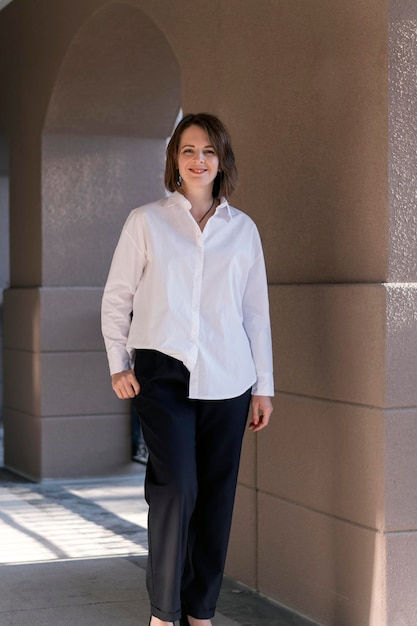 Uma jovem sorridente moderna em negócios casual A garota usa calças de camisa branca e saltos