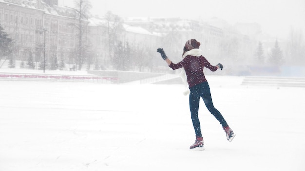 Uma jovem sorridente patinando no gelo diante de uma forte nevasca