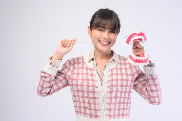 Uma jovem sorridente segurando aparelho invisalign sobre estúdio de fundo branco