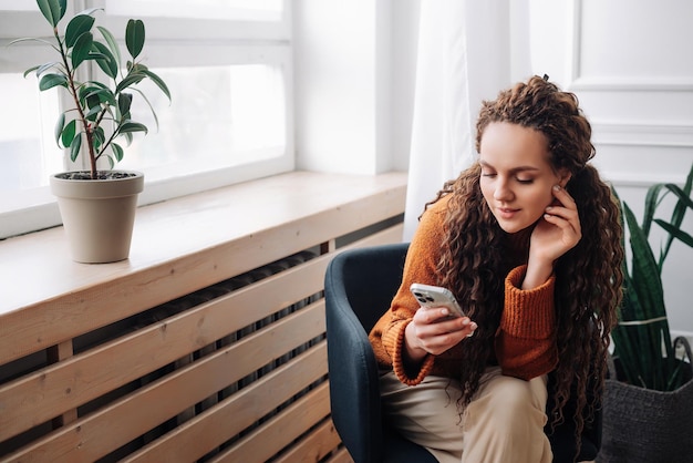 Uma jovem sorridente sentada na cadeira segurando o celular usando um dispositivo de celular olhando para