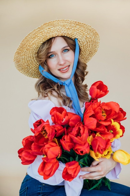 Uma jovem tem um buquê de tulipas vermelhas nas mãos O conceito de 8 de março Dia dos Namorados Um presente maravilhoso para uma menina Retrato de primavera de uma mulher com um chapéu de palha