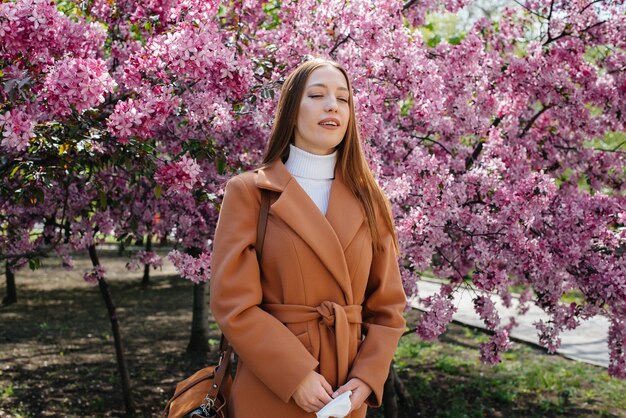 Uma jovem tira a máscara e respira fundo após o fim da pandemia em um dia ensolarado de primavera, em frente a jardins floridos. proteção e prevenção cobertas 19.