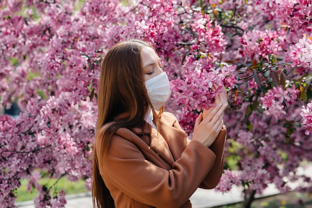 Uma jovem tira a máscara e respira profundamente após o final da pandemia em um dia ensolarado de primavera, em frente a jardins florescendo. Proteção e prevenção covid-19.