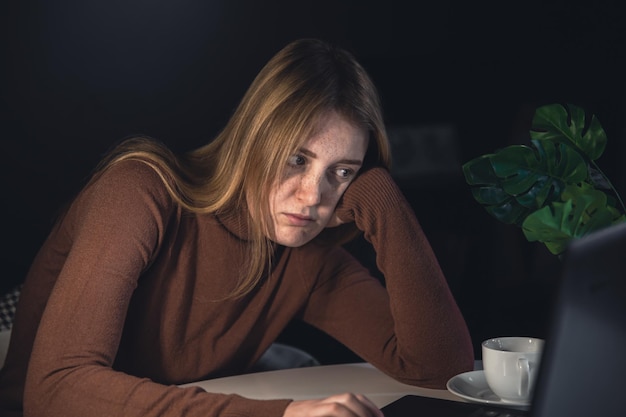 Uma jovem trabalha atrás de um laptop à noite com uma lâmpada