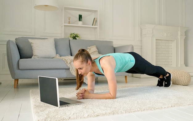 Uma jovem treinando online através do treino remoto do laptop em casa durante a quarentena.