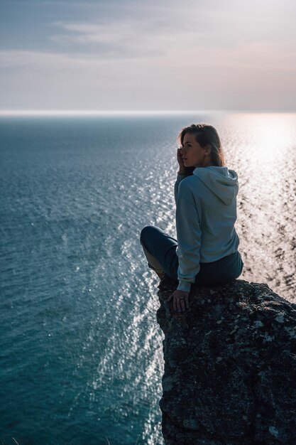 Uma jovem turista apreciando o pôr do sol sobre a paisagem montanhosa do mar enquanto está sentada ao ar livre ioga feminina