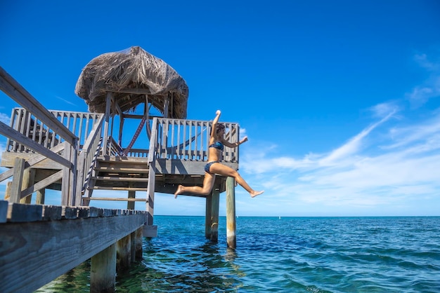 Uma jovem turista se jogando no mar do Caribe na ilha de Roatan de um píer de madeira Honduras