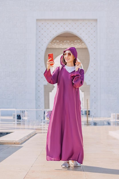 Uma jovem turista vestida com uma Abaya tradicional documenta sua peregrinação pela Grande Mesquita Sheikh Zayed com uma selfie