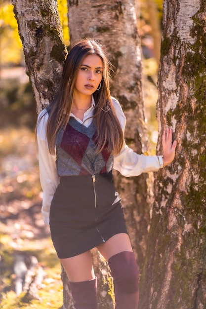 Uma jovem universitária morena caucasiana em um parque ao lado de uma árvore