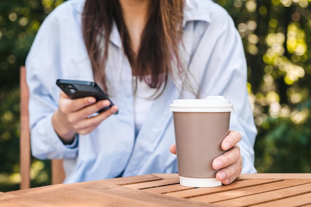 Uma jovem usa um smartphone e segura uma xícara de café na mão