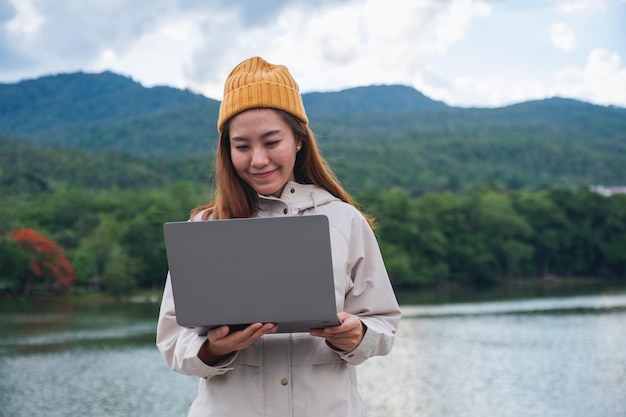 Uma jovem usando e trabalhando no computador portátil enquanto viaja pelas montanhas e lago