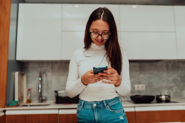 Uma jovem usando um smartphone enquanto cozinha na cozinha