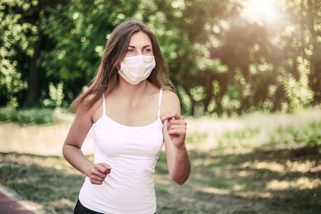 Uma jovem usando uma máscara respiratória protetora corre pelo parque ensolarado e olha para o espaço da cópia, quarentena, covid-19