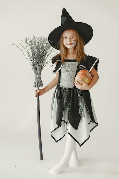 Foto uma jovem vestida de preto como uma bruxa tem um chapéu em forma de cone na cabeça. menina segurando uma vassoura e uma abóbora