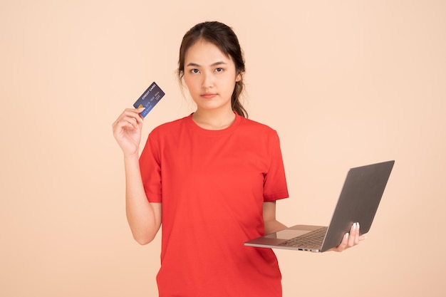 Uma jovem vestindo uma camisa vermelha segura um cartão de crédito e usa um laptop