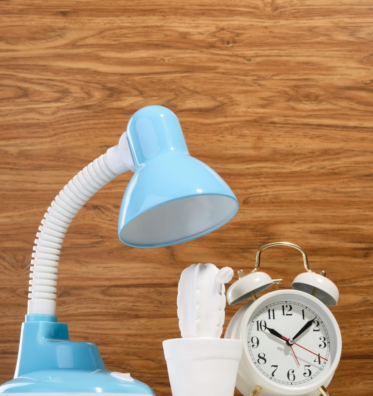 Foto uma lâmpada de mesa azul, um despertador retro vintage e uma estatueta de cacto branco em uma mesa.