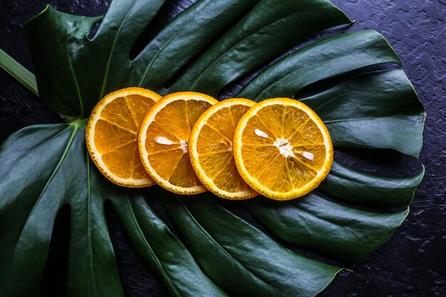 Uma laranja na folha verde tropical. Monstera planta de casa em fundo preto. Foto ecológica.