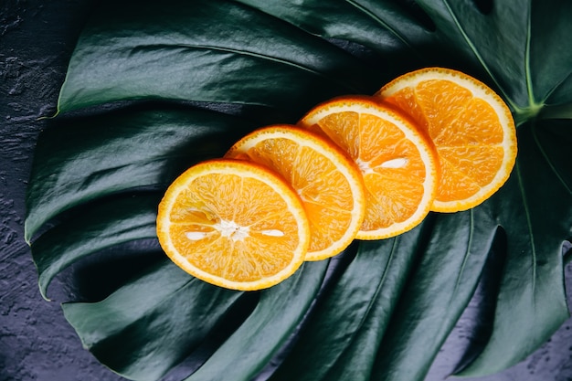 Uma laranja na folha verde tropical. Monstera planta de casa em fundo preto. Foto ecológica.