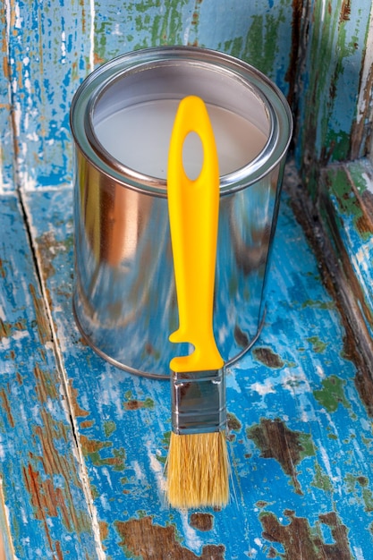 Foto uma lata aberta de tinta branca e um pincel amarelo em uma janela de madeira limpa de tinta velha fechada