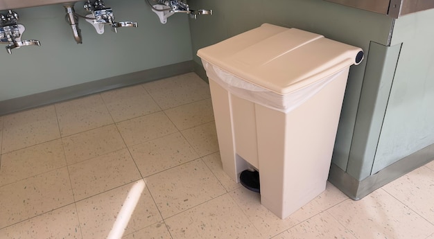 Uma lata de lixo em um banheiro com um saco de lixo branco no chão.