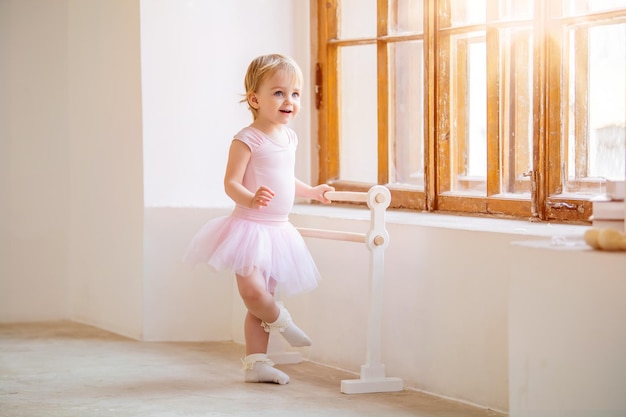 Uma linda bailarina de olhos azuis em um collant rosa e tutu em pé perto de uma barra de balé conceito de sonho de se tornar uma bailarina