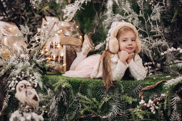 Uma linda criança caucasiana com longos cabelos loiros fica em uma atmosfera de natal com várias árvores decoradas ao seu redor