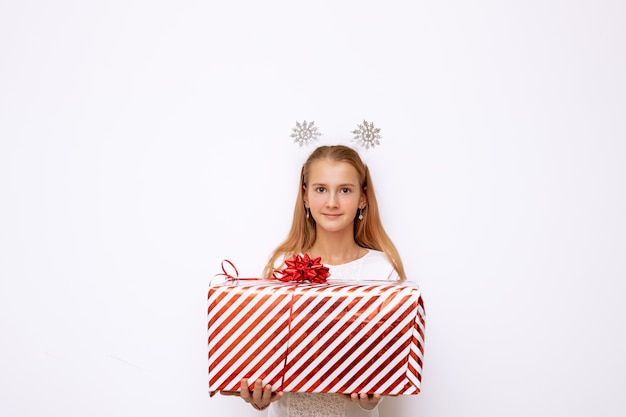 Uma linda criança garota segurando uma caixa de presente listrado vermelho de Natal com uma fita e um laço nas mãos. Existem flocos de neve na cabeça. Isolado