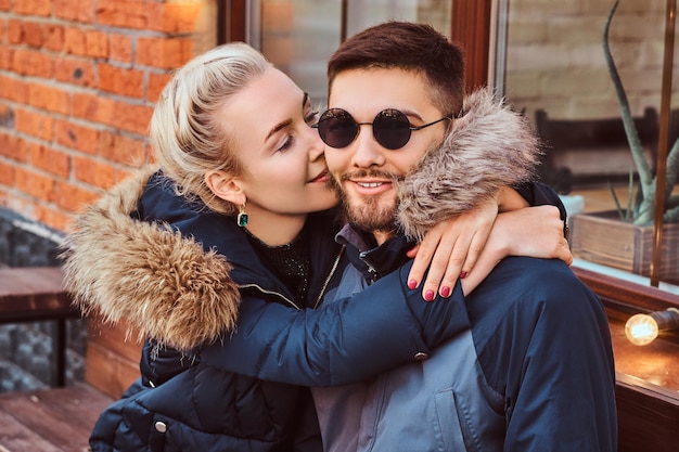 Uma linda garota abraça e beija o namorado enquanto eles estão sentados juntos em um banco perto do café.