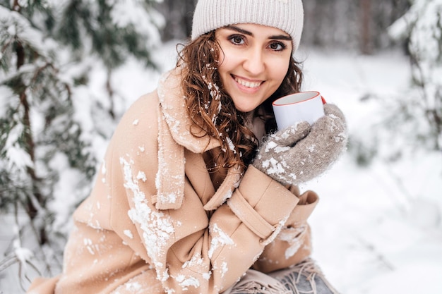 Uma linda garota bebe chá quente no inverno na rua em uma caneca branca e sorri