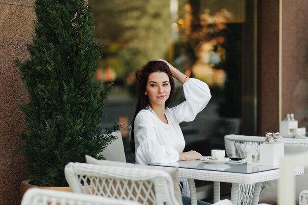 Uma linda garota bonita em um café bebe café em uma mesa.