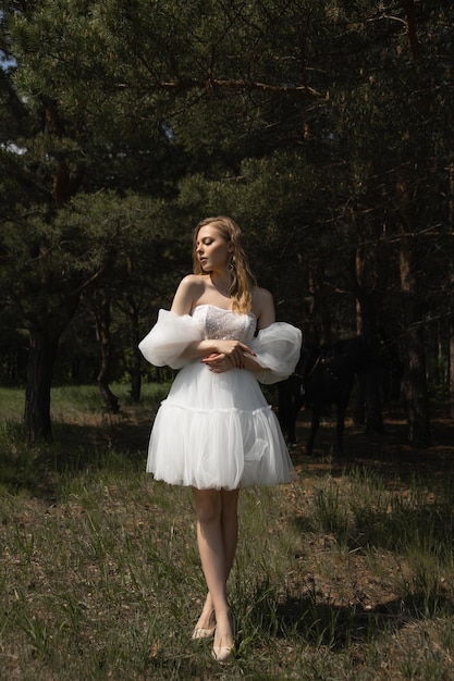 Foto uma linda garota caucasiana em um vestido de noiva fica na floresta sob a luz do sol
