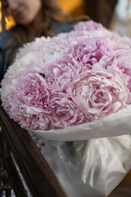 Uma linda garota caucasiana em uma roupa casual com um buquê de peônias de flores fica nas escadas de uma cafeteria de rua